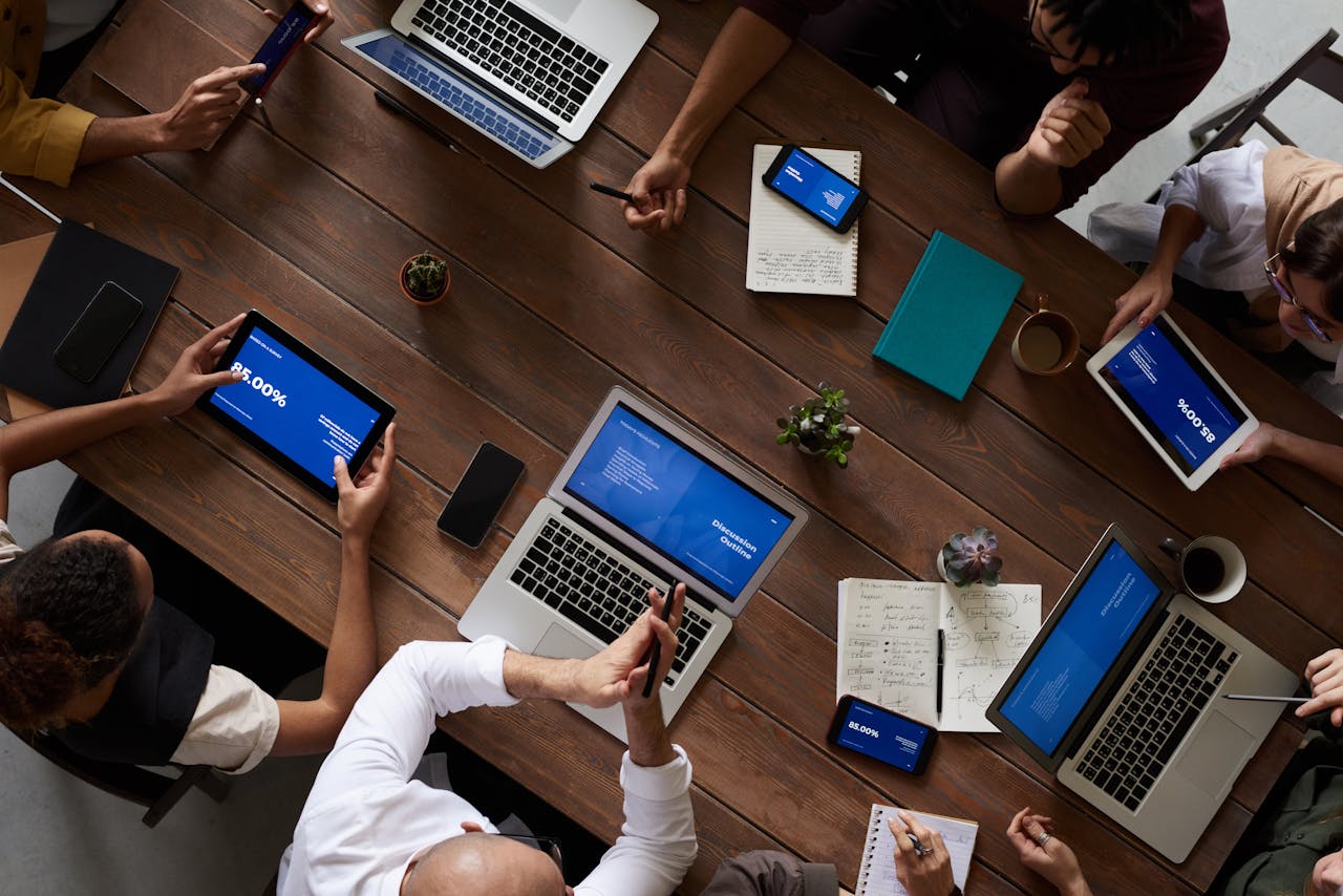 contact-img Overhead view of a diverse team discussing around a wooden table, using technology.